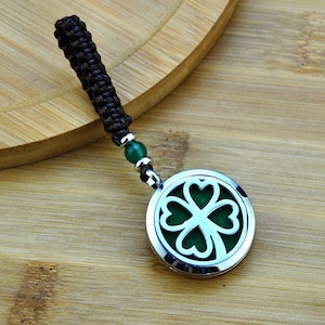 May include: A silver four-leaf clover diffuser pendant with a brown cord and green bead. The pendant is on a wooden surface.