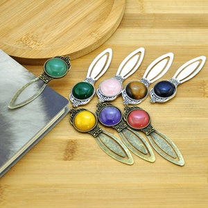 Puede incluir: Conjunto de siete marcapáginas de metal plateado con piedras de vidrio de colores. Cada marcapáginas presenta una piedra de color diferente, incluyendo verde, rosa, marrón, azul, amarillo, morado y rojo.