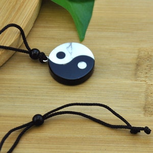 May include: A black and white yin yang pendant necklace with a black cord. The pendant is made of stone and has a white swirl on the black side and a black swirl on the white side.