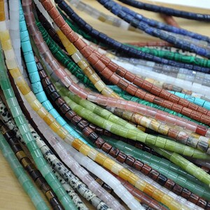 May include: Assortment of colorful gemstone beads, each strand featuring a different type of stone. The beads are square-shaped and have a polished finish. The colors include green, blue, red, brown, white, and yellow.