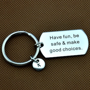 May include: Silver keychain with a tag that reads "Have fun, be safe & make good choices."  The keychain also has a small charm with the letter "K" on it.