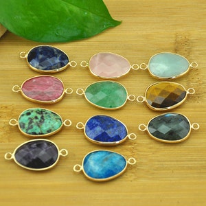 May include: A collection of teardrop-shaped gemstone pendants in various colors, including blue, pink, green, and yellow. Each stone is set in a gold-colored bezel with small loops for attaching to a chain or other jewelry component. The gemstones have a faceted cut.