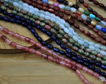 May include: Assortment of oval-shaped beads in various colors, including pink, blue, green, and brown. The beads are strung together, creating multiple strands. The beads are displayed on a wooden surface.
