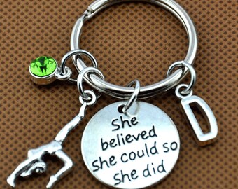 Op de afbeelding: Zilveren sleutelhanger met een turnster-bedel, een groene strasssteen en een ronde bedel met de tekst "She believed she could so she did".