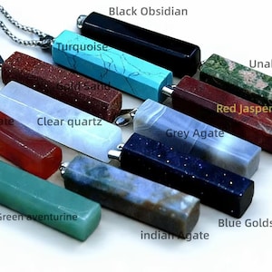 Könnte beinhalten: Eine Auswahl an Edelsteinanhängern in verschiedenen Farben, darunter schwarzer Obsidian, Türkis und roter Jaspis. Jeder Anhänger ist rechteckig mit einer silberfarbenen Metallkappe und an einem schwarzen Band oder einer silbernen Kette befestigt. Die Namen der Edelsteine sind beschriftet.