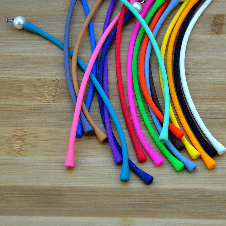 May include: A collection of flexible, smooth, multi-colored silicone cords arranged in a fan shape. Each cord features a small, round, white pearl-like bead at one end, providing a decorative accent to the vibrant array of blue, pink, orange, yellow, black, and white strands.