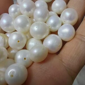 May include: A collection of loose, round, white pearls with a smooth, lustrous finish. Each individual pearl features a small, centered drill hole, indicating they are intended for use as beads in jewelry making or other decorative craft projects.