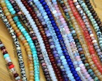 May include: A collection of beaded strands in various colors and materials. The strands include beads labeled as Amethyst, Red Agate, Light Blue Jade, and others. The beads are round and appear to be strung together for jewelry making.