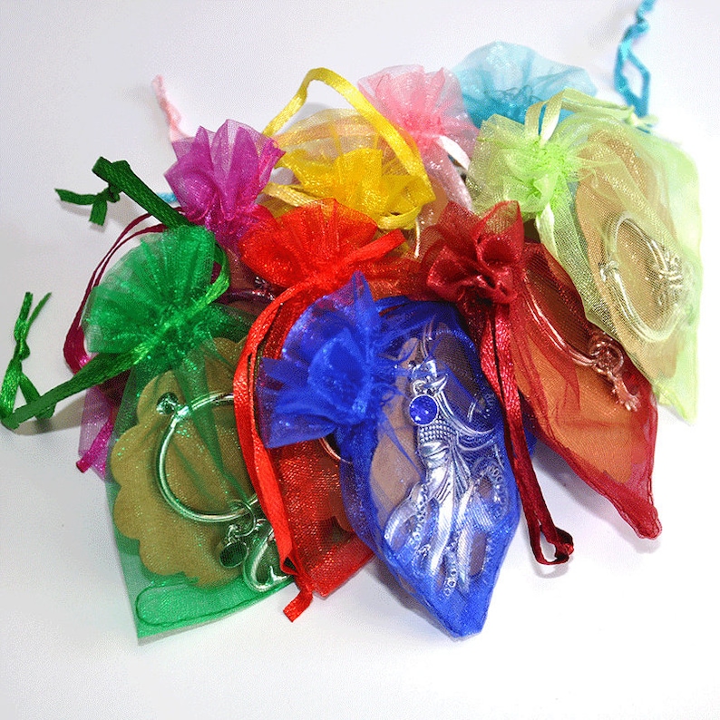 May include: A collection of small, colorful organza bags tied with matching ribbons. The bags contain various charms and keychains, including a silver-toned mermaid, a key, and a heart-shaped charm. The bags are in shades of red, blue, green, yellow, and pink.
