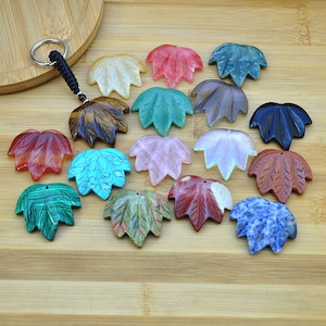 Puede incluir: Una colección de 16 abalorios de hoja de piedra preciosa en varios colores, incluyendo rojo, verde, azul, marrón y rosa. Los abalorios están tallados en forma de hoja de cinco puntas y tienen un agujero en la parte superior para sujetarlos a un collar o pulsera.