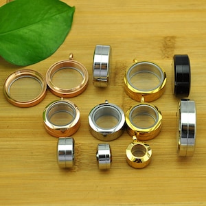 Op de afbeelding: Assortiment van ronde, metalen hanger met transparante glazen inzetstukken. De hangers zijn in verschillende afwerkingen verkrijgbaar, waaronder goud, zilver en rosé goud.