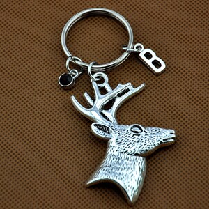 May include: Silver-toned deer head keychain with a black rhinestone charm and a silver letter 'B' charm attached to a silver key ring.