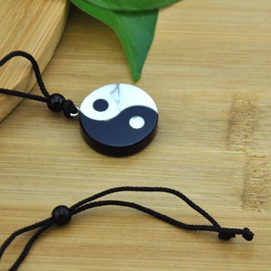 May include: A black and white yin yang pendant necklace with a black cord. The pendant is made of stone and has a marbled effect.