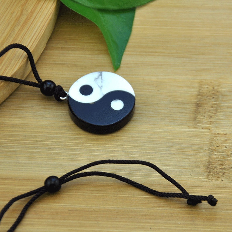 May include: A black and white yin yang pendant necklace with a black cord. The pendant is made of stone and has a marbled effect.