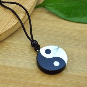 May include: Black and white yin yang pendant necklace with a black cord. The pendant is made of stone and has a marbled effect.