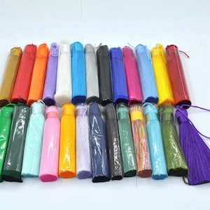 May include: Assortment of colorful tassel trims in various colors, including red, orange, purple, blue, green, yellow, white, and black. The tassels are packaged in clear plastic sleeves.