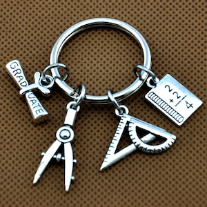 Può includere: Portachiavi di laurea argentato con un diploma, un compasso, un goniometro e un ciondolo con l'equazione 22/4.