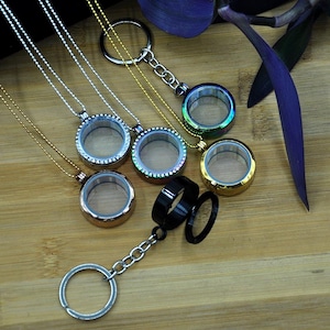 May include: Five silver, gold, and black locket necklaces with clear glass inserts. The lockets are round and have a decorative border. The necklaces are on a wooden surface.