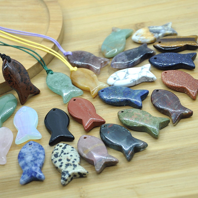 May include: A collection of 20 gemstone fish pendants in various colors and patterns, including red, green, blue, black, white, and brown. The pendants are made of natural stones and are strung on cords.