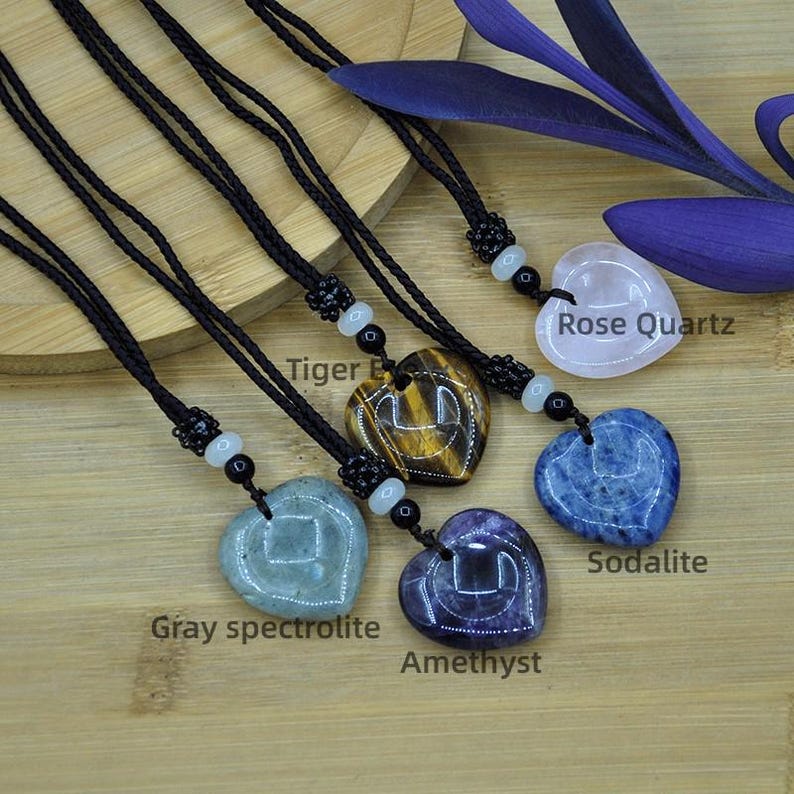 May include: Heart-shaped gemstone pendants on black cords. The pendants are made of rose quartz, sodalite, amethyst, tiger eye, and gray spectrolite. Each pendant has a unique color and pattern. The gemstones are labeled with their names.