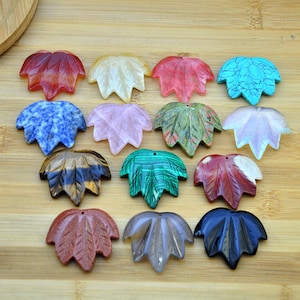 Könnte beinhalten: Sortiment von 15 geschnitzten Ahornblatt-Anhängern aus Edelsteinen in verschiedenen Farben, darunter Rot, Blau, Grün, Braun, Rosa, Weiß und Schwarz.