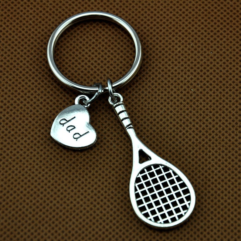 Puede incluir: Llavero de raqueta de tenis de plata con un dije de coraz&oacute;n que dice "pap&aacute;".