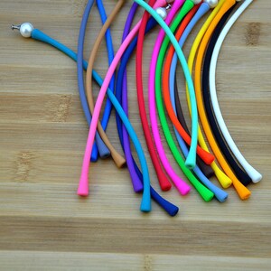 May include: A collection of flexible, smooth silicone cords in a variety of vibrant colors including blue, pink, orange, green, yellow, black, and white. Each cord features a small, round, white pearl-like bead attached to one end.