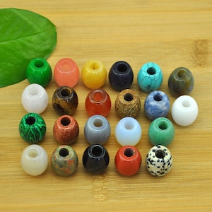 Pode incluir: Conjunto de 20 contas redondas de pedras preciosas em várias cores, incluindo verde, vermelho, azul, marrom, branco, preto e amarelo. As contas são lisas e polidas, com um furo no centro para enfiar.