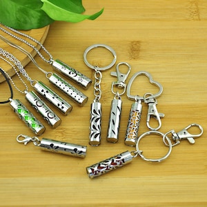 Puede incluir: Un conjunto de difusores de aceite esencial de metal plateado con varios diseños. Algunos están unidos a collares y otros a llaveros. Los difusores son cilíndricos y tienen intrincados recortes.