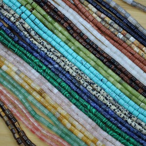 May include: A variety of gemstone beads in different colors and patterns, including turquoise, green, blue, brown, and white. The beads are all cylindrical in shape and are arranged in rows.