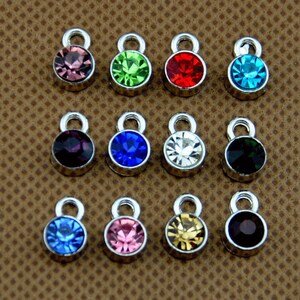 May include: Twelve silver charm pendants with different colored rhinestones. The charms have a small loop at the top for attaching to a bracelet or necklace.
