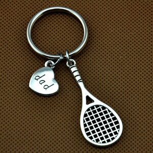 Puede incluir: Llavero de plata con un dije de raqueta de tenis y un dije de coraz&oacute;n que dice "pap&aacute;".