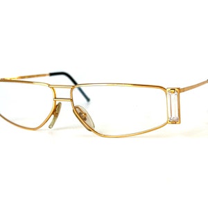 May include: Gold-tone metal eyeglasses with clear lenses and rectangular frames. The frames have clear crystal accents on the sides.