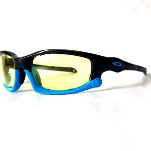 May include: Black and blue wraparound sunglasses with yellow lenses. The sunglasses have a sporty design and are ideal for outdoor activities.