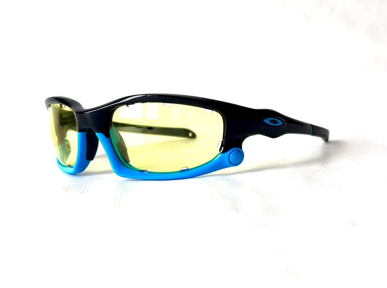 May include: Black and blue wraparound sunglasses with yellow lenses. The sunglasses have a sporty design and are ideal for outdoor activities.