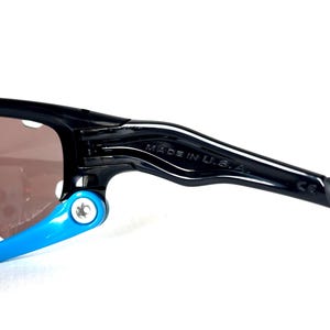 May include: Black sunglasses with blue accents and a brown lens. The sunglasses have a "MADE IN U.S.A." label on the arm.