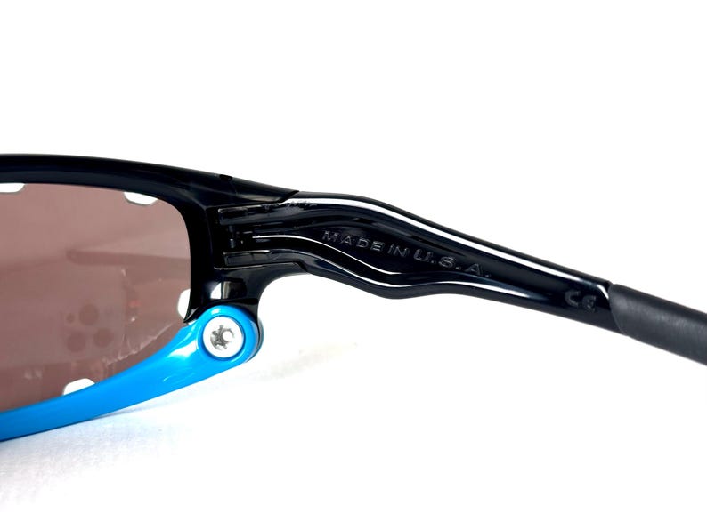 May include: Black sunglasses with blue accents and a brown lens. The sunglasses have a "MADE IN U.S.A." label on the arm.