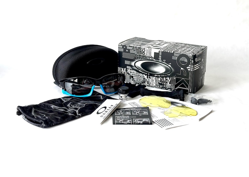 May include: Black Oakley sunglasses with blue accents, a black case, and a variety of accessories, including a cleaning cloth, a small bottle of cleaning solution, and a spare lens.