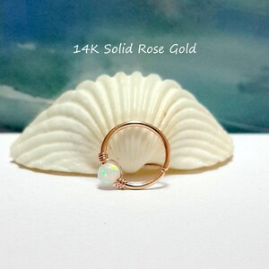 May include: A 14K solid rose gold hoop earring with a white opal gemstone. The earring is on a white seashell background.