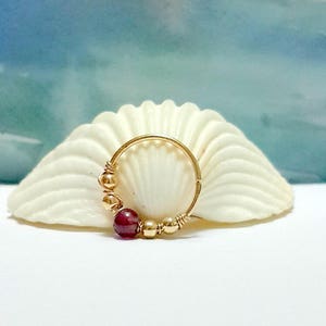 May include: Gold hoop earring with a single red gemstone and gold beads.