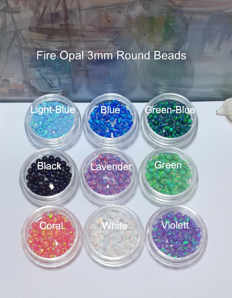 May include: Assortment of 3mm round fire opal beads in various colors, including light blue, blue, green-blue, black, lavender, green, coral, white, and violet. The beads are displayed in small clear containers.