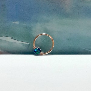 May include: A gold hoop earring with a blue and green gemstone. The hoop is made of metal and the gemstone is set in a wire wrap.