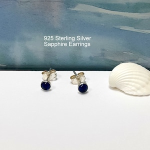 May include: A pair of sterling silver stud earrings with small, round, dark blue sapphire stones.