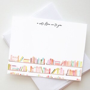 Peut inclure: Une carte blanche avec le texte "a note from me to you" imprimé en haut. Le bas de la carte présente une illustration aquarelle d'une bibliothèque remplie de livres colorés.