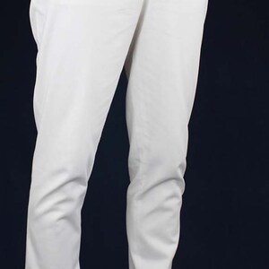 May include: White pants with a button fly and suspenders. The pants are made of a lightweight fabric and have a relaxed fit. The person is wearing black shoes with white accents.
