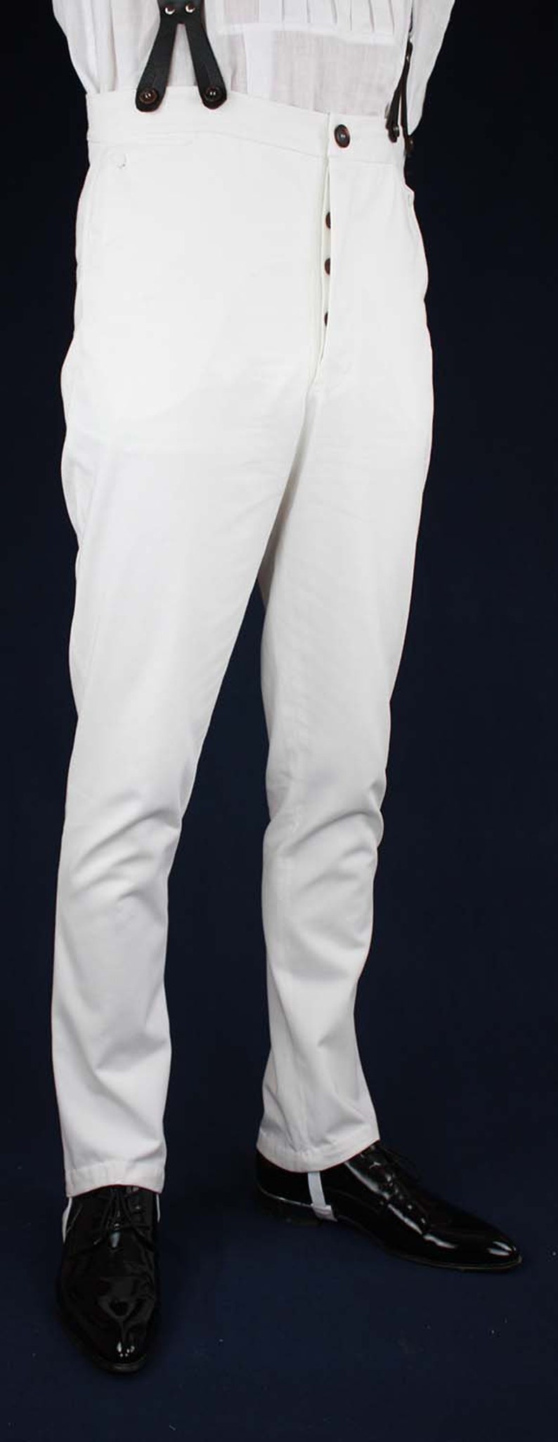 May include: White pants with a button fly and suspenders. The pants are made of a lightweight fabric and have a relaxed fit. The person is wearing black shoes with white accents.