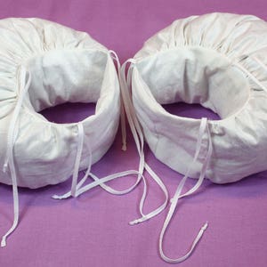 May include: Two white fabric headbands with adjustable ties. The headbands are made of a soft, white fabric and have a gathered design.