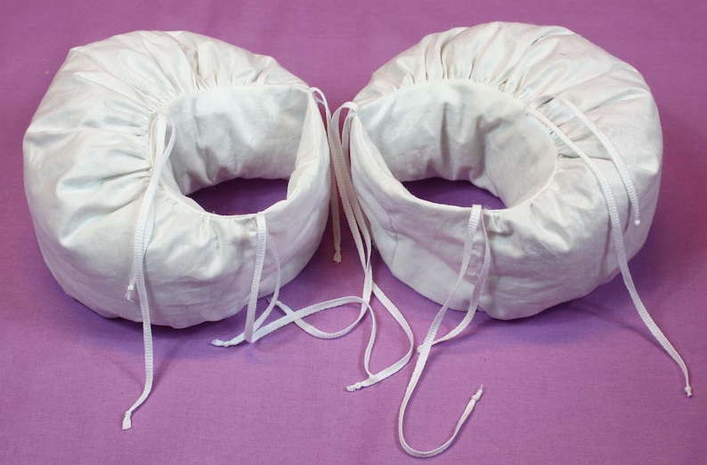 May include: Two white fabric headbands with adjustable ties. The headbands are made of a soft, white fabric and have a gathered design.