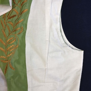 May include: A green vest with a white lining and gold embroidery of leaves. The vest has a button closure and a pointed collar.
