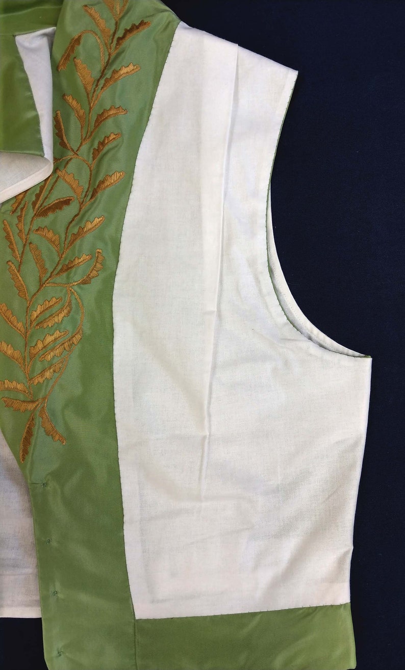 May include: A green vest with a white lining and gold embroidery of leaves. The vest has a button closure and a pointed collar.